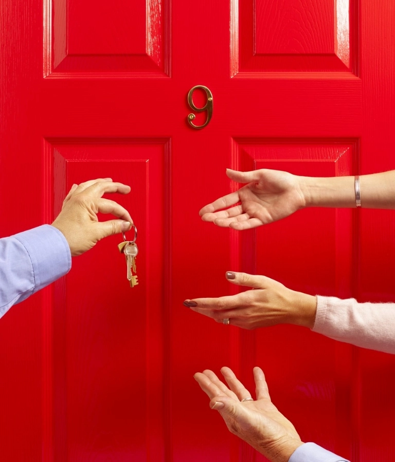 Wyciągnięte dłonie i dłoń trzymająca klucze na tle czerwonych drzwi